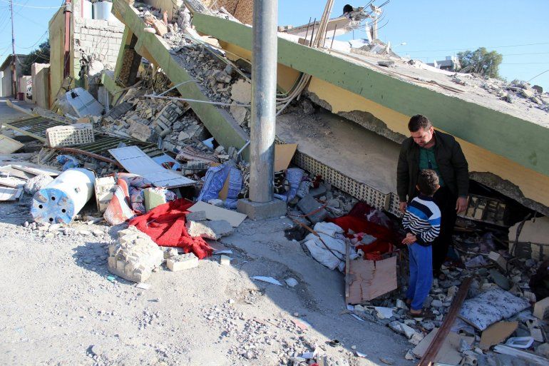 Un hombre unto a un ni&ntilde;o permanecen al lado de las ruinas de un edificio que colaps&oacute; durante el terremoto. 