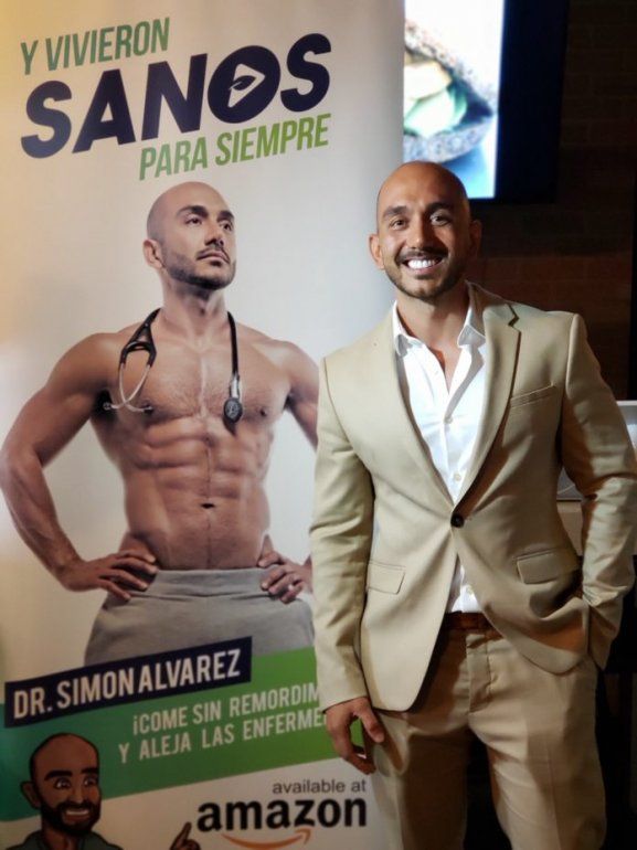 Fotograf&iacute;a del m&eacute;dico cirujano Sim&oacute;n &Aacute;lvarez frente a la imagen de portada de su libro "Y vivieron sanos para siempre", publicada el 