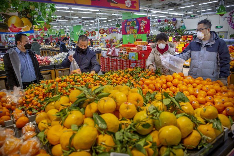 Varias personas compran cítricos en un supermercado de Beijing, protegidos por una mascarilla facial, en Beijing, China, el 28 de enero de 2020. 