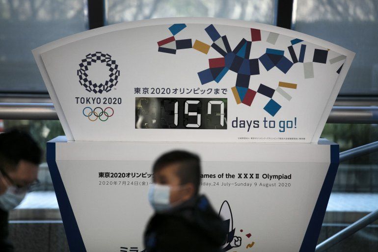 En esta fotografía del martes 18 de febrero de 2020, unas personas que portan mascarillas caminan frente a un reloj de cuenta regresiva para los Juegos Olímpicos en Tokio. 