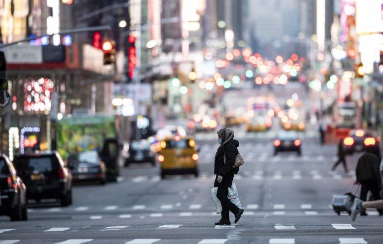 Una mujer con una m&aacute;scara cruza la calle en Times Square en Manhattan el 17 de marzo de 2020 en la ciudad de Nueva York. El brote de coronavirus ha transformado a los Estados Unidos pr&aacute;cticamente de la noche a la ma&ntilde;ana de un lugar de consumo ilimitado a uno repentinamente limitado por la anidaci&oacute;n y el distanciamiento social. 