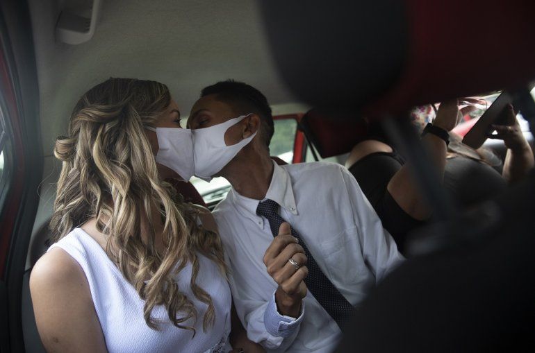 Con mascarillas para evitar la propagaci&oacute;n del coronavirus, Thiago do Nascimento (derecha) y Keilla de Almeida se besan durante su boda, en el drive-thru de un registro en el vecindario de Santa Cruz, R&iacute;o de Janeiro, Brasil, el 28 de mayo de 2020. Las parejas comenzaron a recurrir a esta forma poco convencional de contraer matrimonio en una notar&iacute;a en Santa Cruz desde el inicio de la pandemia en el pa&iacute;s. 