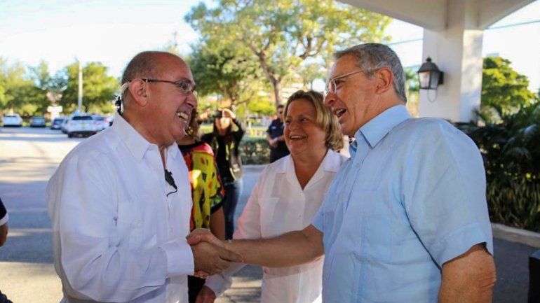 El expresidente Álvaro Uribe (der.) estrecha su mano al activista colombiano Fabio Andrade. Observa la excongresista federal Ileana Ros-Lehtinen.