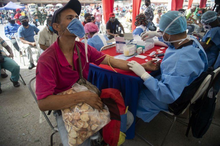 Un trabajador de salud le toma una muestra de sangre para una prueba r&aacute;pida de COVID-19 a un hombre que trabaja vendiendo galletas en el mercado de alimentos de Coche en Caracas, Venezuela, el martes 23 de junio de 2020.