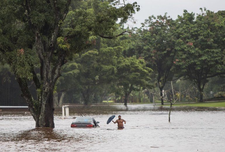El propietario de un coche, prácticamente sumergido, intenta rescatar objetos personales de su interior, en una avenida afectada por las inundaciones provocadas por el paso del huracán Lane en Hilo, Hawái, Estados Unidos. 