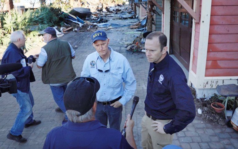El gobernador de la Florida, Rick Scott (cen.), habla a los medios durante un recorrido por Mexico Beach, uno de los lugares más afectados tras el paso del huracán Michael.
