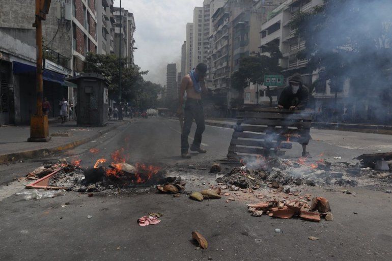 Dos manifestantes levantan una barricada en la avenida Baralt.