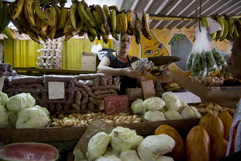 Una mujer cuenta dinero luego de vender unas verduras a un cliente en su puesto en La Habana, Cuba, el miércoles 30 de julio de 2019.