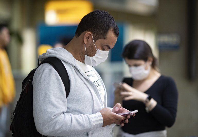 Pasajeros usando mascarillas como precaución contra el contagio del nuevo coronavirus usan sus teléfonos en el Aeropuerto Internacional de Sao Paulo, Brasil, el jueves 27 de febrero de 2020. 