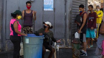 Las personas usan mascarillas como medida preventiva contra la pandemia mundial de coronavirus COVID-19 mientras esperan para recoger agua de una tubería de la calle en Caracas, el 27 de marzo de 2020.     