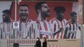 En esta foto del 5 de mayo de 2020, dos mujeres con mascarillas pasan frente a un afiche gigante con la imagen de jugadores del Atlético de Madrid en el estadio Wanda Metropolitano. En esta foto del 5 de mayo de 2020, dos mujeres con mascarillas pasan frente a un afiche gigante con la imagen de jugadores del Atlético de Madrid en el estadio Wanda Metropolitano.