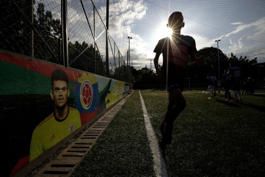 Jóvenes futbolistas entrenan en el Club Bayer de fútbol escolar, fundado por Luis Manuel Díaz, padre del jugador de la selección de Colombia y del equipo inglés Liverpool, Luis Díaz, representado en una pintura en la pared a la izquierda, en Barrancas, Colombia, el miércoles 8 de noviembre de 2023.
