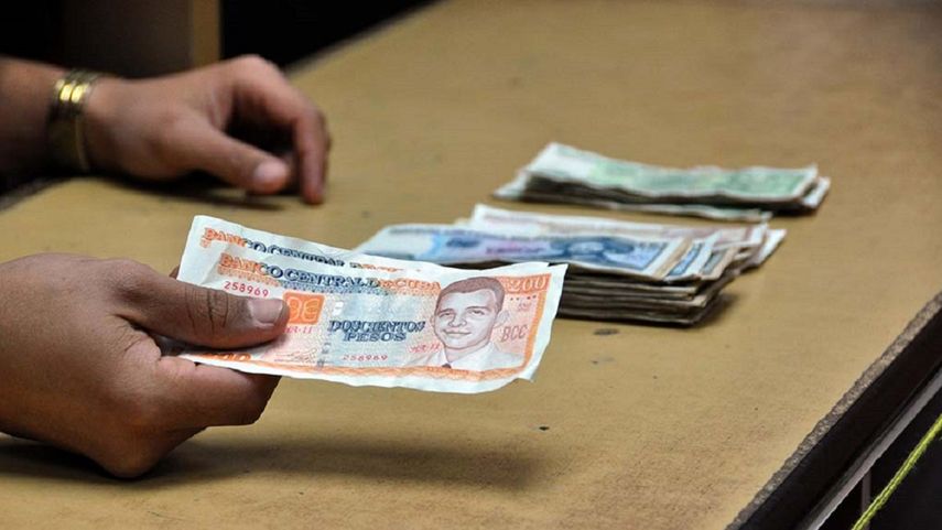 Fotografía de archivo de una persona que sostiene pesos cubanos convertibles (cuc) sobre una mesa con pesos cubanos (cup).