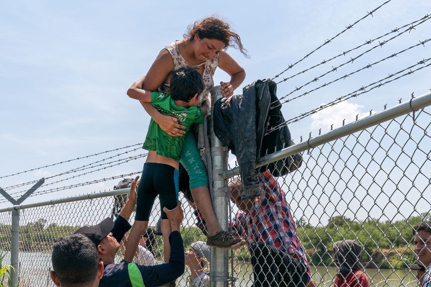 Una madre ayuda a su hijo a pasar la valla de alambre de púas en Eagle Pass, Texas, después de cruzar a Estados Unidos desde México el 25 de agosto de 2023. UNICEF alertó sobre la magnitud de la crisis de migración infantil en América Latina y el Caribe.