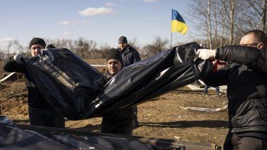 Varios hombres cargan con una bolsa que contiene los restos de un cadáver recién exhumado, en un cementerio a las afueras de Borodyanka, Ucrania, el 2 de marzo de 2023.&nbsp; 