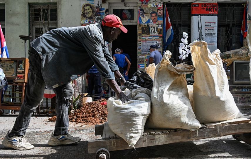Un hombre transporta objetos cerca de una casa que muestra un cartel del depuesto dictador venezolano Nicolás Maduro y del fallecido Hugo Chávez, en La Habana el 14 de enero de 2026.