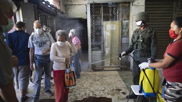 Una mujer de edad avanzada, con una m&aacute;scara facial protectora, es rociada con una soluci&oacute;n desinfectante de cloro por un soldado como medida preventiva contra la propagaci&oacute;n del nuevo coronavirus COVID-19, a la entrada de un mercado de alimentos en Caracas, Venezuela, el viernes 20 de marzo de 2020.&nbsp;