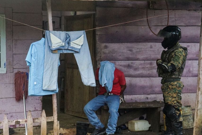 Un detenido se sienta con las manos esposadas por un miembro del Servicio Nacional de Fronteras (SENAFRONT) en las afueras de Santa Fe, en la provincia de Darién, Panamá, el miércoles 7 de agosto de 2024. La policía fronteriza de Panamá arrestó a presuntos traficantes de chinos que ingresan por la selva de Darién en su camino a Estados Unidos. 