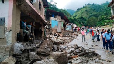 En esta foto proporcionada por la oficina de prensa del gobierno del estado de Mérida, personas caminan por una calle dañada por inundaciones y deslizamientos de tierra provocados por lluvias torrenciales en la zona del Valle del Mocoties del municipio de Tovar en el estado de Mérida, Venezuela.