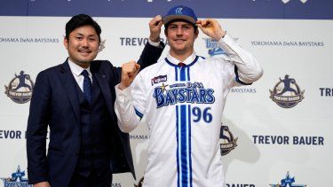 Trevor Bauer porta el uniforme y gorra del Yokohama DeNA BayStars junto al director de operaciones del equipo, Tatsuhiro Hagiwara, en la conferencia de prensa de su presentación, el viernes 24 de marzo del 2023.