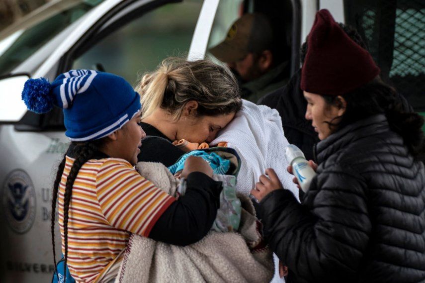Una solicitante de asilo nicaragüense (izquierda) carga a su sobrino de dos meses antes de dárselo a su madre (derecha) mientras una solicitante de asilo cubana besa a su hijo de cuatro años mientras esperan que un agente de la Patrulla Fronteriza tome su información, en Eagle Pass, Texas el 19 de diciembre de 2022.