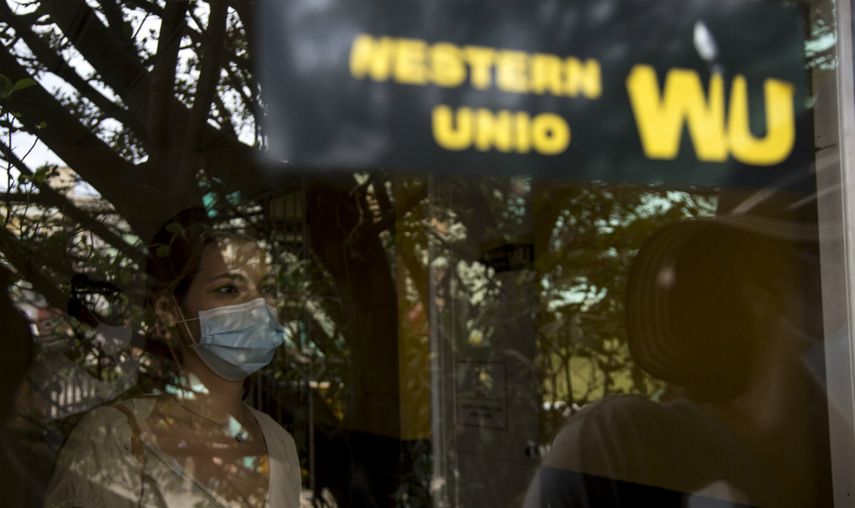 Fotografiada a través de una ventana, una mujer aguarda a cobrar en una oficina de Western Union durante su último día de operaciones en La Habana, Cuba, el lunes 23 de noviembre de 2020. Cuba iniciará un reordenamiento económico profundo a partir del 1 de enero que incluirá la unificación monetaria y cambiaria, así como un aumento de cinco veces en los salarios.