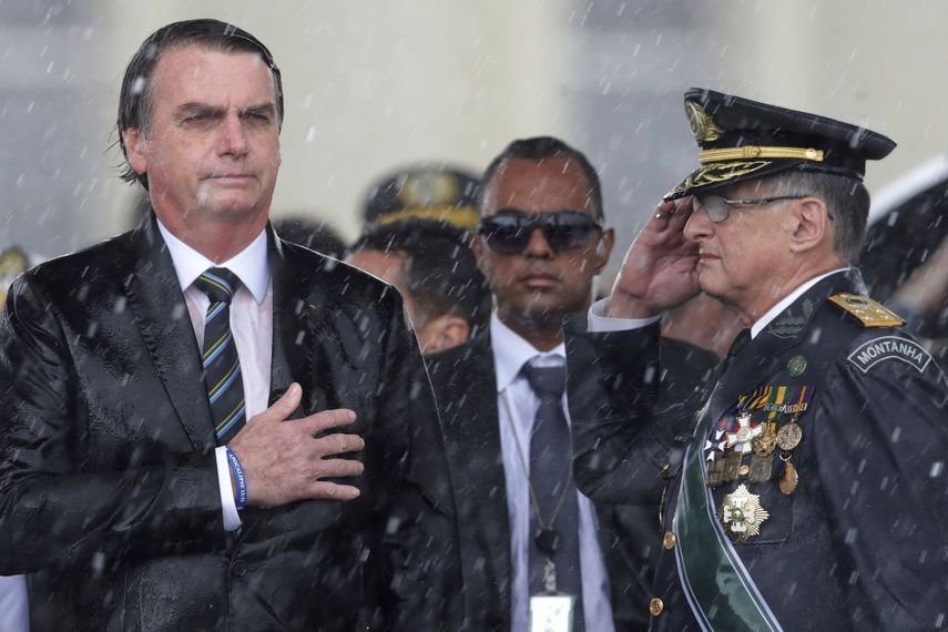 En esta imagen de archivo, el presidente de Brasil, Jair Bolsonaro, se lleva la mano al corazón y el comandante del ejército brasileño Edson Leal Pujol hace un saludo militar durante la interpretación del himno en una ceremonia, celebrada bajo un intenso aguacero, para conmemorar el Día del Ejército, en Brasilia, Brasil. En el inicio de su segundo año como presidente, Bolsonaro se ha mantenido firme en sus combativas políticas mientras se enfrentó a sus críticos tanto dentro como fuera del país.&nbsp;