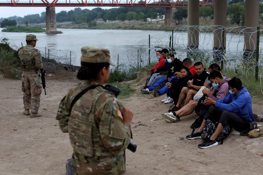 Varios migrantes que cruzaron el río Bravo hacia Estados Unidos bajo la custodia de miembros de la Guardia Nacional mientras esperan la llegada de agentes de la Patrulla Fronteriza en Eagle Pass, Texas, el viernes 20 de mayo de 2022.&nbsp;
