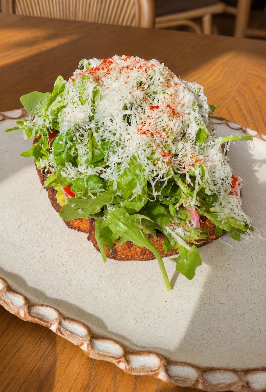 Rúcula y una generosa capa de queso rallado cubren la tostada de aguacate.