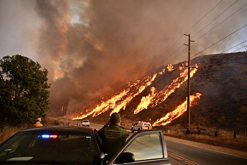 Un alguacil observa cómo las llamas suben por la colina mientras la columna de humo del incendio Hughes llena el cielo en Castaic, un barrio del noroeste de Los Ángeles, California, el 22 de enero de 2025. Un nuevo incendio forestal estalló al norte de Los Ángeles el 22 de enero, creciendo en tamaño y provocando miles de órdenes de evacuación en una región que ya se tambaleaba por los efectos de enormes incendios.