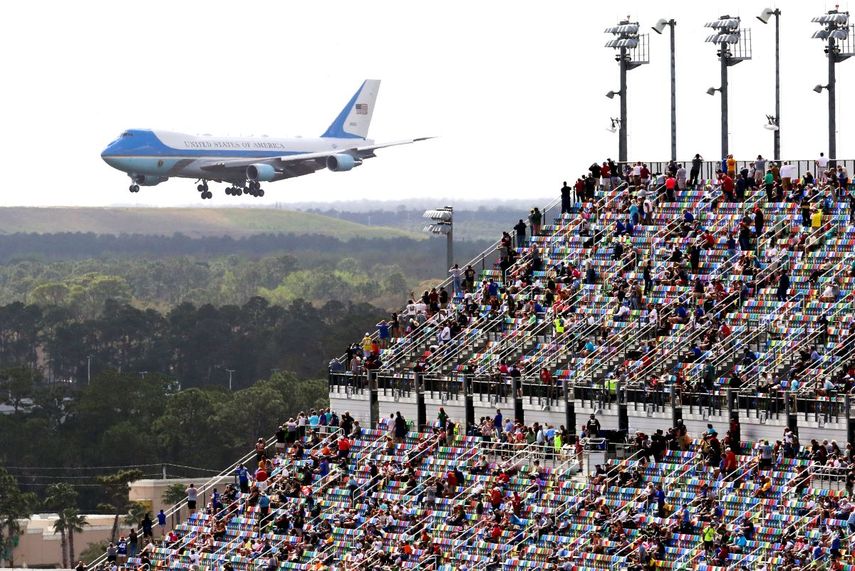 Aficionados de las carreras observan desde las gradas cuando el avión Air Force One da una vuelta sobre el circuito Daytona mientras el presidente Donald Trump llega para asistir a la carrera de autos NASCAR Daytona 500 en la Daytona International Speedway el domingo 16 de febrero de 2020 en Dayton Beach, Florida. 