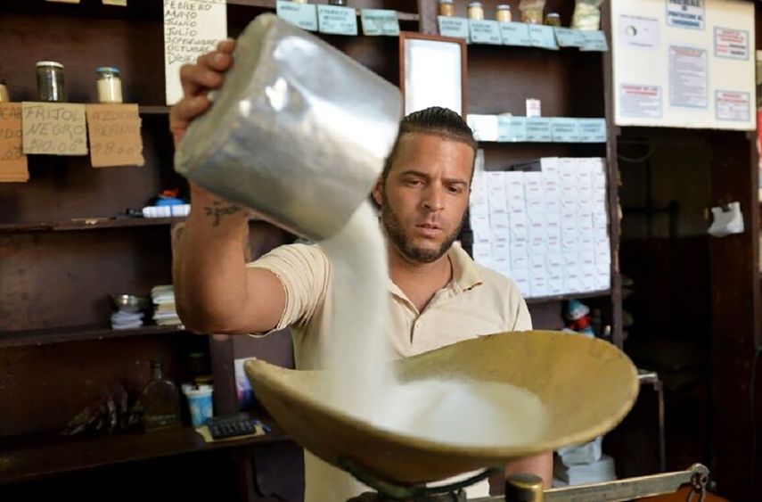 Azúcar, un empleado de tienda deposita el preciado producto en una pesa, Cuba.