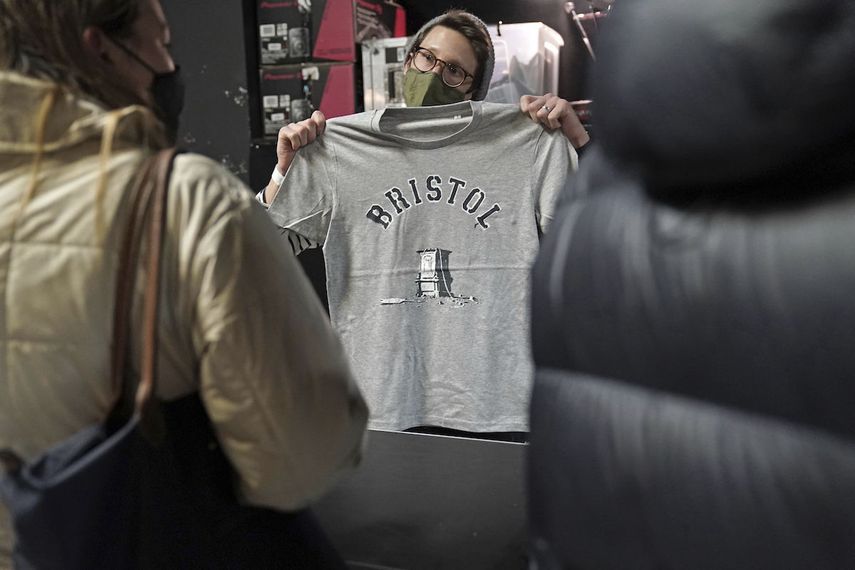 Una persona dentro de Rough Trade en Bristol, Inglaterra, sábado 11 de diciembre de 2021, muestra una camiseta diseñada por el artista callejero Banksy, en venta para apoyar a cuatro personas juzgadas por daños criminales por estar implicadas en derribar la estatua del comerciante de esclavos Edward Colston.