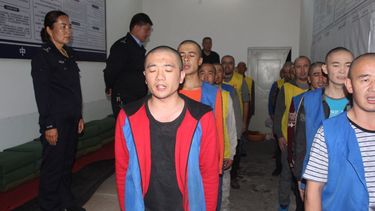 La Fundación Conmemorativa de las Víctimas del Comunismo muestra a los detenidos custodiados por la policía mientras hacen fila aparentemente recitando o cantando en el centro de detención del condado de Tekes en la región de Xinjiang, en el oeste de China.