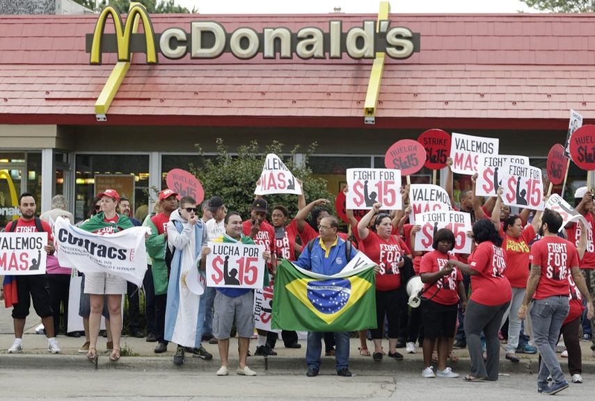 Empleados de un restaurante de comida rápida en Chicago exigen con carteles un aumento del salario mínimo a $15 por hora. Miami-Dade será sede hoy de una protesta similar. (AP)