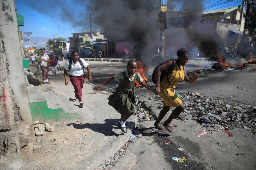Una mujer y su hija pasan corriendo frente a una barricada levantada por la policía en protesta por el mal gobierno policial en Puerto Príncipe, Haití, el 26 de enero de 2023.