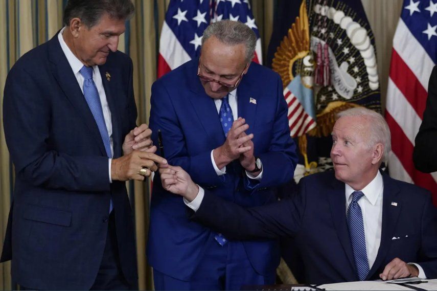 El presidente Joe Biden ofrece un lapicero al senador demócrata Joe Manchin durante una cena en la Casa Blanca. En el centro el jefe de la mayoría demócrata en el Senado, Chuck Shumer. Agosto de 2022.
