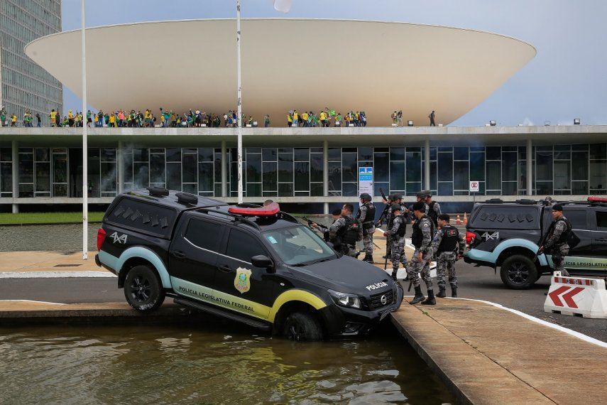 Miembros de la Policía Federal Legislativa junto a un vehículo que se estrelló contra una fuente cuando los partidarios del expresidente brasileño Jair Bolsonaro invaden el Congreso Nacional en Brasilia el 8 de enero de 2023.&nbsp;&nbsp;