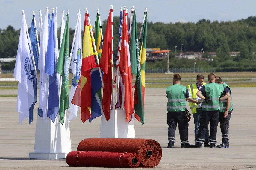 Operarios esperan junto a banderas y alfombras rojas preparadas en el aeropuerto para la llegada de los líderes de los estados que acudirán a la cumbre del G20, en&nbsp;Hamburgo.