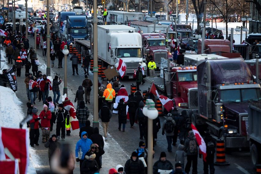 Personas caminan junto a camiones estacionados en la calle Wellington durante una manifestación contra las restricciones del COVID-19 en el Parlamento, en Ottawa, el sábado 29 de enero de 2022.&nbsp;