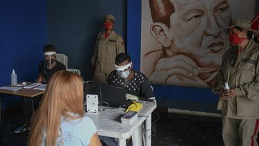 Personal del Consejo Nacional Electoral (CNE) con equipo protector del coronavirus revisa archivos en Caracas, Venezuela, con miras a las elecciones legislativas del 6 de diciembre. Detrás suyo hay una imagen de Hugo Chávez. 