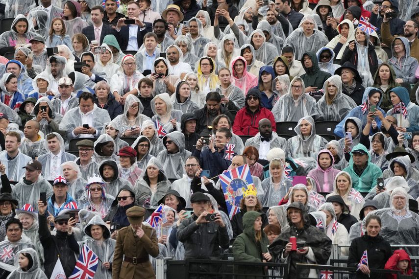 Gente bajo la lluvia en tribunas junto al Palacio de Buckingham antes de la ceremonia de coronación del rey Carlos III de Gran Bretaña en Londres, el sábado 6 de mayo de 2023.
