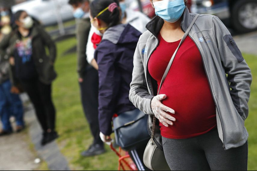 En esta fotografía de archivo del jueves 7 de mayo de 2020, una mujer embarazada que utiliza mascarilla y guantes por la pandemia de coronavirus hace fila con numerosas personas para recibir una despensa de alimentos financiada por la organización caritativa Healthy Waltham en la iglesia St. Mary en Waltham, Massachusetts.