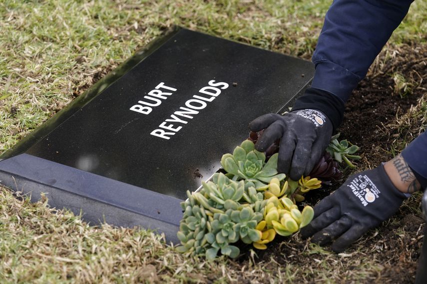 Un trabajador coloca flores frente a una lápida temporal para el difunto actor Burt Reynolds en la sección Jardín de Leyendas del cementerio Hollywood Forever, el jueves 11 de febrero de 2021 en Los Ángeles.