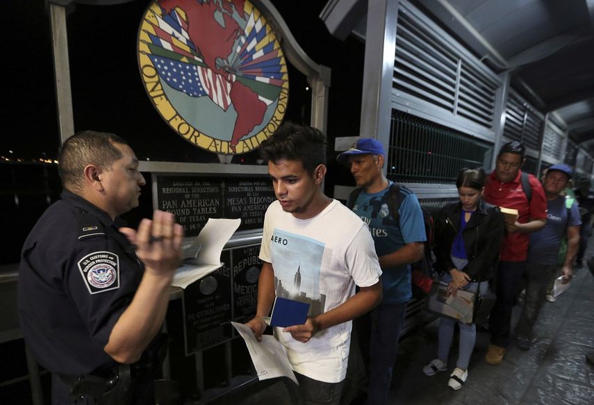 El cubano Abel Oset hijo, al centro, y su padre Abel Oset, detrás de él, muestran sus identificaciones a un agente de la Oficina de Aduanas y Protección Fronteriza de EEUU en el cruce del puente internacional 1 de Nuevo Laredo, México, antes de su cita para solicitar asilo en Estados Unidos.