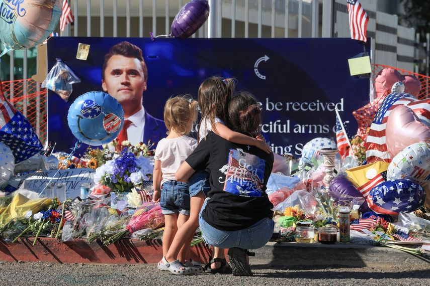 Una madre y sus dos hijas rinden tributo a Charlie Kirk frente a una foto suya situada en la entrada de la sede de su organización Turning Point USA en Arizona.