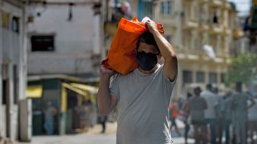 Un hombre sostiene una bolsa con comida en una calle en La Habana. Al fondo, un grupo de personas espera en una fila.