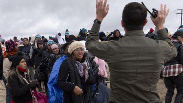 La peruana Julia Paredes, a la izquierda con un gorro blanco, escucha las instrucciones de un agente de la patrulla fronteriza junto a otros solicitantes de asilo, mientras esperan a ser procesados tras cruzar la cercana frontera con México, el jueves 25 de abril de 2024, en Boulevard, California.&nbsp;