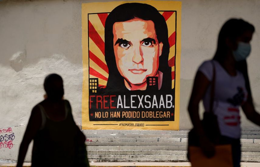 Personas caminan cerca de un cartel que pide la liberación del empresario colombiano, Alex Saab, en Caracas, Venezuela.