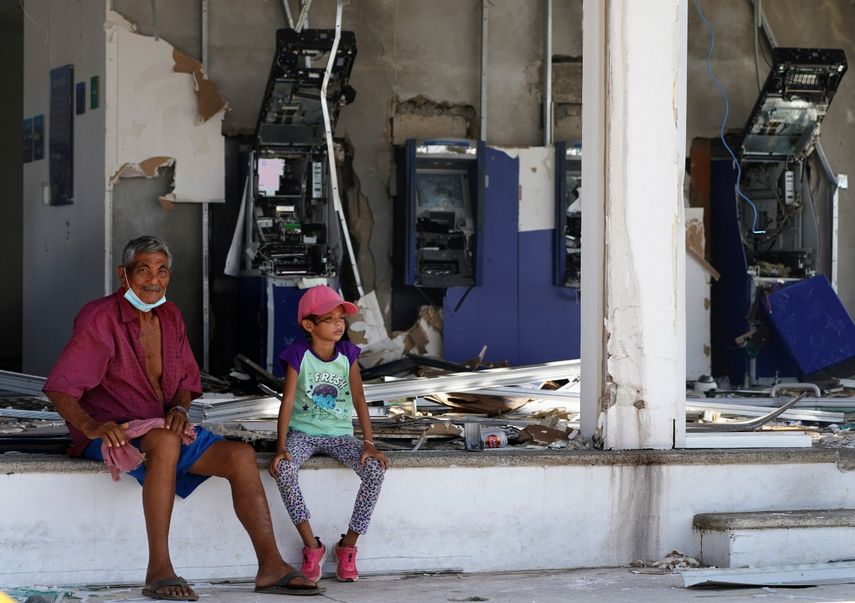 Residentes sentados delante de una entidad bancaria, sin ventanales y con los cajeros destrozados, dos días después del paso del devastador huracán Otis, de categoría 5, en Acapulco, México, el viernes 27 de octubre de 2023.